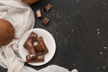 Plate with tasty chocolate covered coconut candies on black background