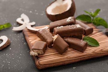 Wooden board with tasty chocolate covered coconut candies on black background