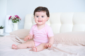 Fototapeta premium portrait of smiling healthy baby in pink bodysuit on bed