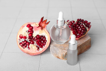 Composition with bottles of essential oil, stone and pomegranate on light tile table