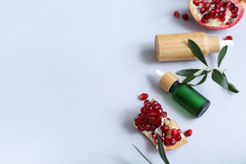 Composition with bottles of essential oil and ripe pomegranate on light background
