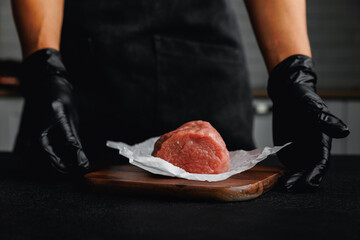Butcher woman hold fresh meat veal fillet on parchment and wooden board, dark background