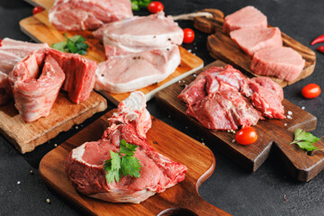 Variety of raw beef meat and pork ribs, pig steaks for grilling with seasoning on wooden board,...