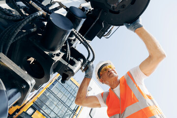 Man in hard hat industrial worker Machinery tractor mechanic checks hydraulic hose system equipment...