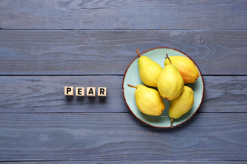 Word PEAR and plate with fresh fruits on blue wooden background