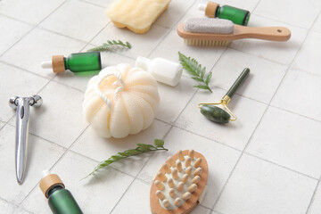 Face massage rollers and bathing supplies on light tile background