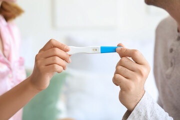 Happy young couple with pregnancy test in bedroom, closeup