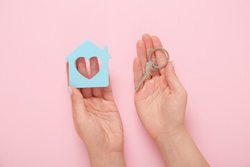 Fototapeta na wymiar Female hands with house figure and key on pink background. Concept of buying real estate