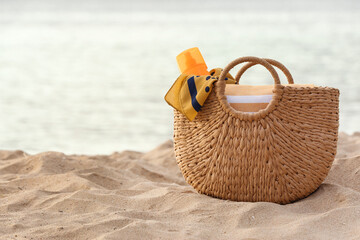 Wicker bag with different beach accessories on sand near ocean at resort