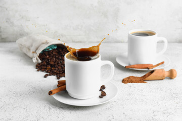Obraz na płótnie Canvas Cup of tasty coffee with splashes and cinnamon on light background