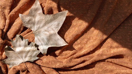 Dry brown fall sycamore leaves on terracotta red, orange knitted folded textile background with...