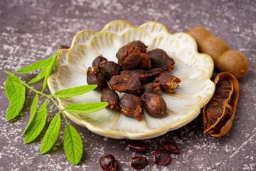 Plate of tasty tamarinds, seeds and leaf on grey background