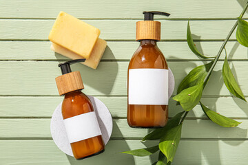 Bottles of shampoo and soap bars on green wooden background