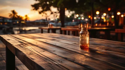 Fotobehang Wooden table top with blurry beach cafés in the backdrop at dusk - suitable for montaging or displaying your goods. © Sawitree88