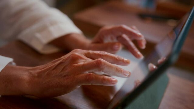 Close-up: female hands typing on a tablet screen in a cafe. Wrinkled fingers themselves touch the touchscreen in a coffee shop or restaurant. Grandma writes a message. Typing text, freelancer.