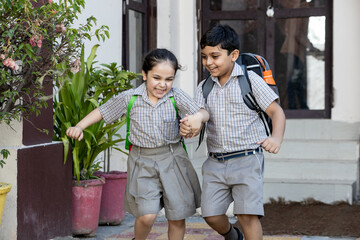 Happy indian school kids student holding hands running outside the primary school. Education concept.