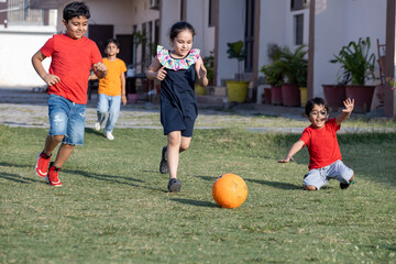 Group of happy Indian kids playing soccer or foot ball at the summer park.