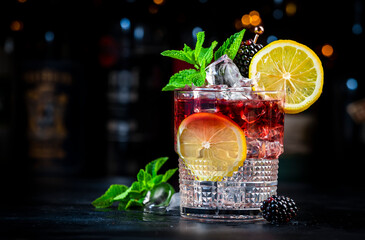 Bramble cocktail drink with dry gin, liqueur, syrup, lemon juice, blackberry, mint and ice. Black...