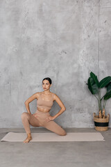 A beautiful young woman with collected hair, dressed in a light sports uniform, poses in the studio against a gray background. Advertising for health, athletic body, yoga clothes, sportswear.