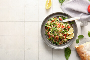 Plate with delicious tabbouleh salad and bread on light tile background