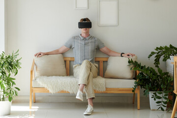 Young man in vr headset sitting on couch at home, watching movie