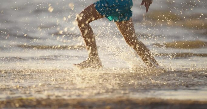 Feet running on the sand on beach, slow motion, cinematic. Concept of kid have fun. Full, happy childhood without childhood trauma. Psychological health. The boy runs raising clouds of splashes