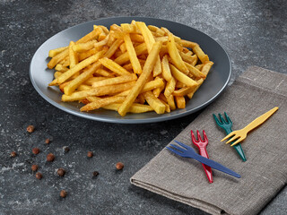 Portion of delicious French fries lying on a plate, served with disposable plastic forks of different colors and a linen napkin. - 651479413