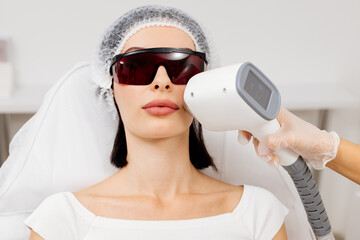 Therapist-cosmetologist performs laser treatment on a woman's face in a beauty spa clinic....