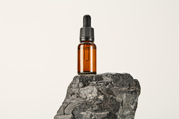 Serum, massage oil in glass dropper bottle on basalt.