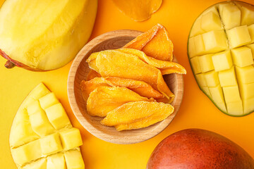 Wooden bowl with slices of dried mango on orange background