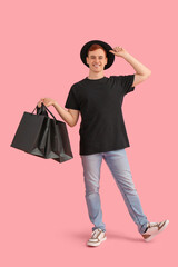 Happy young redhead man with shopping bags on pink background. Black Friday sale