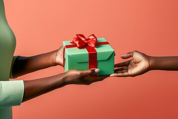 Concept of giving, hand of afro american woman giving green gift box to another afro american girl, isolated on light red background.