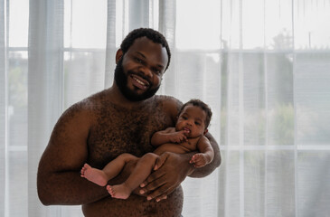 Young black dad with no shirt carrying cute little son baby with love and happiness in the bedroom...