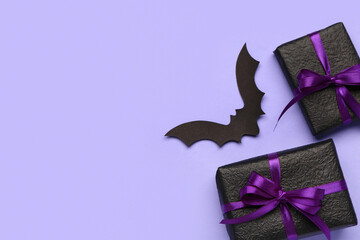 Paper bat for Halloween party and gift boxes on lilac background