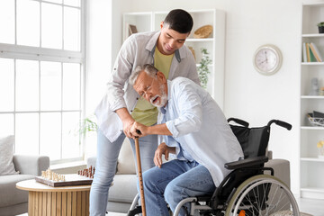 Senior man in wheelchair with stick and his son at home