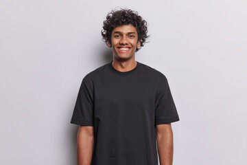 People positive emotions concept. Studio waist up of young happy smiling broadly Hindu man standing in centre isolated on white background wearing black casual t shirt looking straight at camera - 651490085