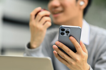 Happy young man eating an apple and using smartphone outside university building