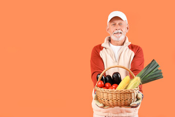 Mature male farmer with wicker basket full of different ripe vegetables on orange background