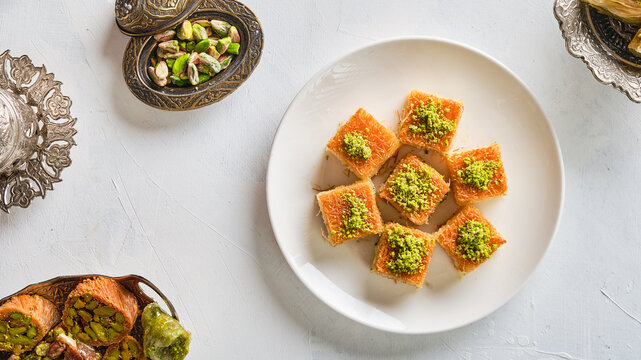 An image taken from above of a plate of Arabic sweets on a white background. Name of the item in Arabic: kunafe