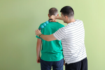 Mature man training with rehabilitation therapist on green background, back view