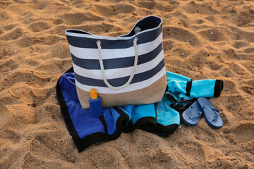 Stylish beach bag, flip-flops, sunscreen cream and towel on sand