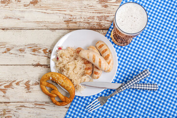 Plate with tasty Bavarian sausages, pretzel, sauerkraut and glass of beer on white wooden background. Oktoberfest celebration