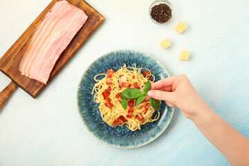 Woman decorating tasty pasta carbonara with basil on white background