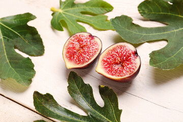 Halves of fresh ripe fig and leaves on white wooden background