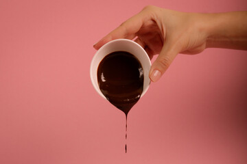 Hand holding a cup with flowing chocolate. Pink background.