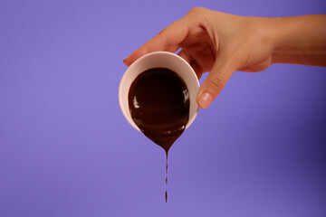 Hand holding a cup with flowing chocolate. Violet background.