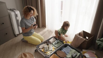 Mother and son packing suitcase together. Family preparation for vacation mother and son with smiles packing bags for exciting adventure. Cooperation of mother and son actively packing travel suitcase