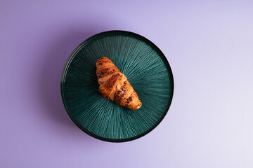 Croissant on the beautiful plate. Violet background. Delicious picture. Minimalistic photography. 