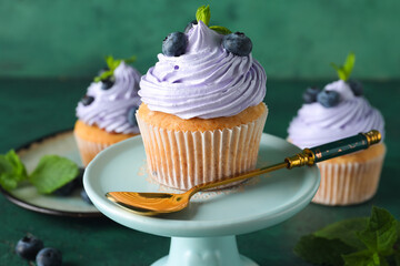 Stand of delicious cupcake with blueberries and mint on green background