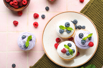 Plate of delicious cupcakes with blueberries, raspberries and mint on pink tile background